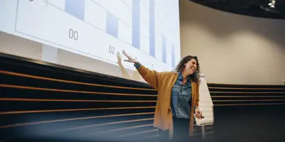 Businesswoman gesturing at projection screen and making a presentation during seminar. Female speaker giving presentation in conference.