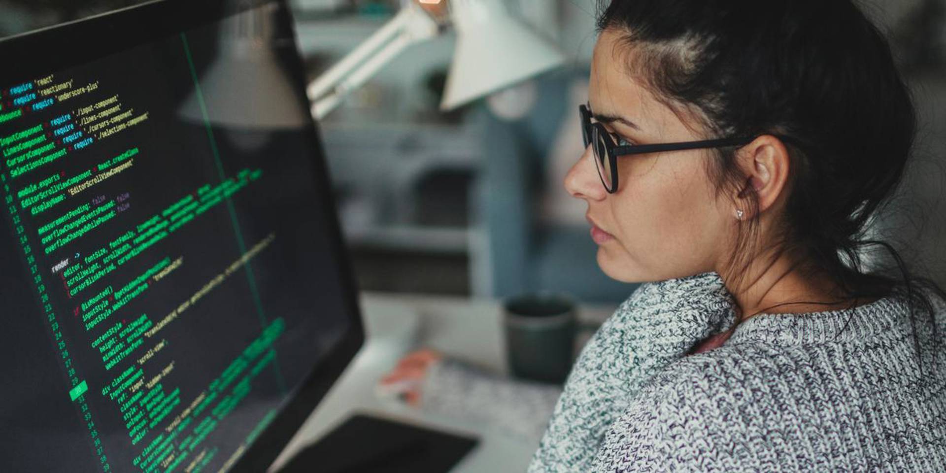 Photo of a young woman sitting at her desktop computer, doing computer programming in her home office